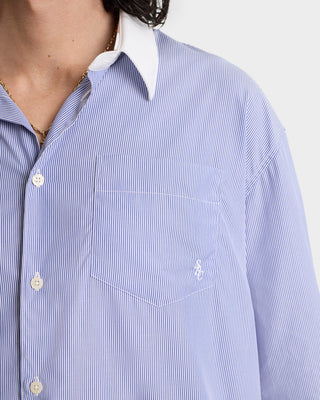 Close-up of a person wearing the SRC Shirt - Blue Striped, an oversized fit blue and white pinstriped button-up with a white collar, made from cotton poplin.