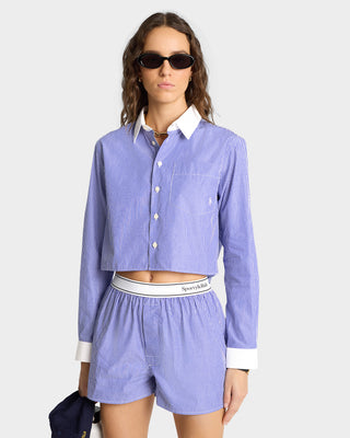 Woman in the Serif Logo Boxer - White/Blue Stripe, a blue-and-white striped cotton boxer with an elastic waistband, paired with a matching cropped shirt and sunglasses, poses against a plain background.