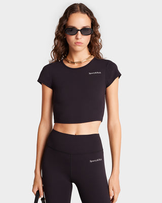 A person in sunglasses is wearing the Serif Logo Training Tee in Black/White and leggings, perfectly embodying the essence of luxury activewear.