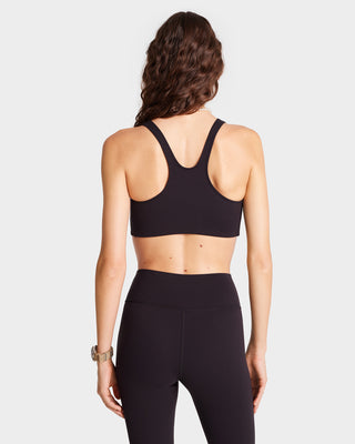 A long-haired person is wearing luxury activewear, featuring the Serif Logo Sport Bra in Black/White, paired with leggings and facing away against a plain background.