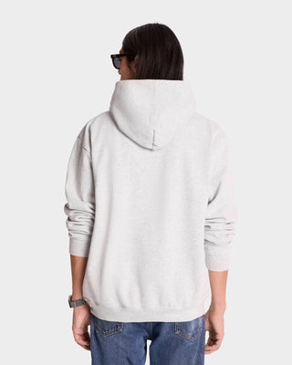 A person in a Serif Logo Hoodie - Heather Gray/Navy, crafted from USA-grown cotton, paired with denim jeans, is seen from the back against a plain backdrop.
