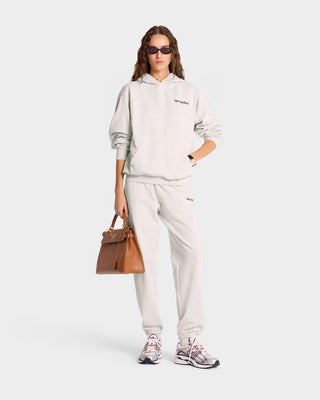 A person wearing a Heather Gray/Navy Serif Logo Hoodie and sunglasses holds a brown handbag, standing against a white background.
