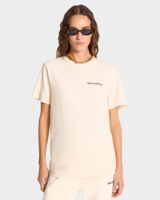 A person wears black sunglasses and a Health is Wealth T-Shirt in cream/navy, made from 100% cotton, with matching pants against a plain background.