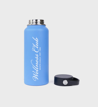 The Wellness Club Bottle - Juniper is a blue insulated water bottle with Wellness Club text. It features a wide mouth and a detachable black screw cap, all set against a white background.
