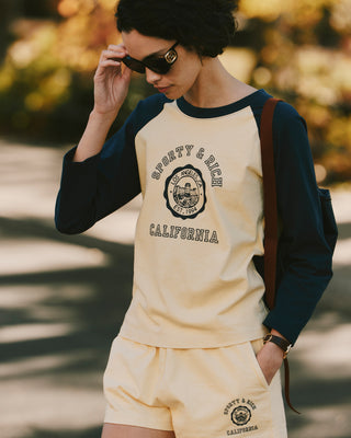 Woman in sunglasses enjoying the outdoors in a yellow Sporty & Rich California Emblem Disco Short - Almond/Navy set with an elastic waistband, made in the USA.