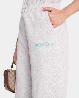 A person wearing Rizzoli Tennis Sweatpant in Heather Gray/Caribbean, featuring the Tennis Club logo and crafted from USA-grown cotton, has a hand in their pocket while holding a brown handbag.
