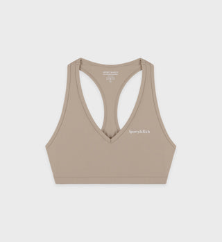 Indulge in luxury activewear with the Serif Logo V Neck Sports Bra in Elephant/White, featuring a chic racerback design and Sporty & Rich elegantly printed in white.