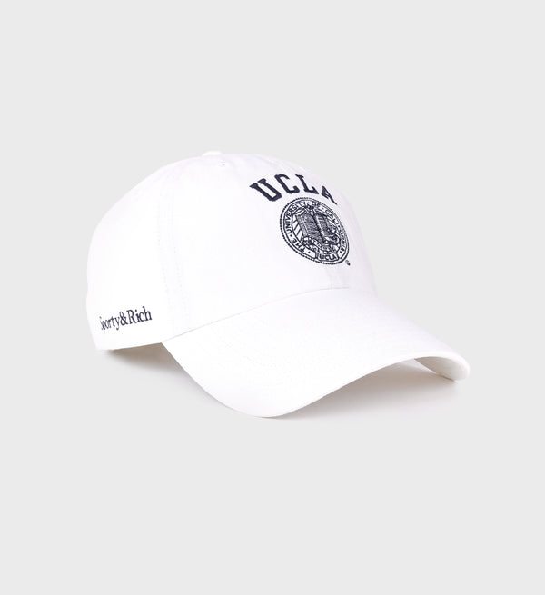 White baseball cap with navy 'UCLA' text and the official UCLA seal embroidered on the front, 'Sporty & Rich' serif logo embroidered on right side, featuring a curved brim.