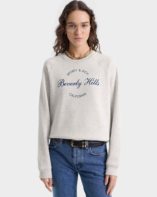 A woman in glasses and jeans stands against a plain background, wearing the Beverly Script Soft Crewneck in Heather Gray/Navy.