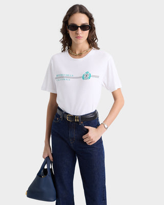 A person in sunglasses wearing the white Beverly Hills Horizon Soft T-Shirt made of 100% cotton, paired with jeans, holds a blue bag against a plain background.