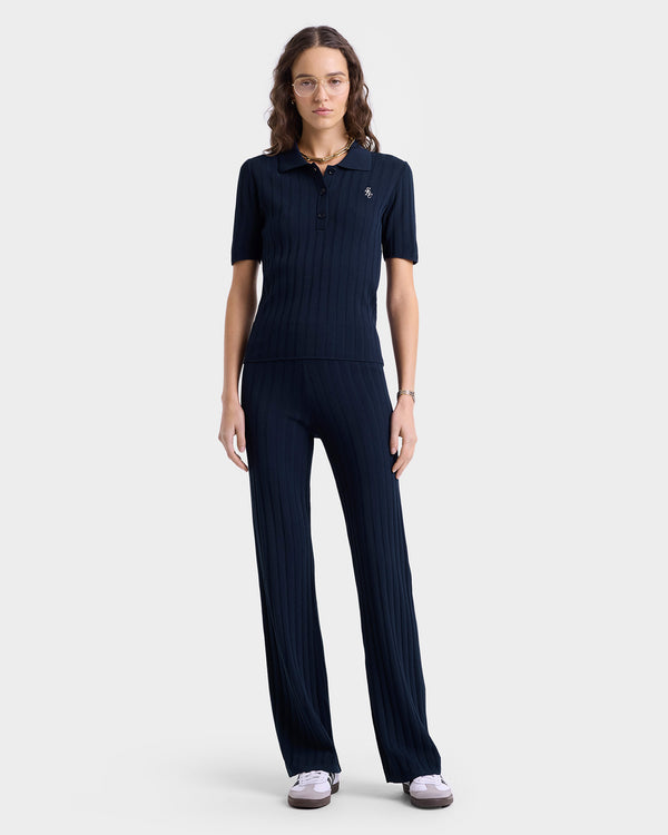 Woman wearing the SRC Ribbed Polo in Navy/White and matching pants, standing against a plain light background.