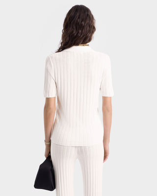Woman with wavy brown hair, shown from the back, wears a cream ribbed top and SRC Ribbed Trousers in Ecru/Navy with an elastic waistband, holding a black handbag.