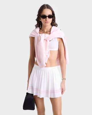 Woman in sunglasses wearing a white crop top and the Vendome Script Pleated Skirt - White/Pink Dolphin, with a pink sweater draped over her shoulders.