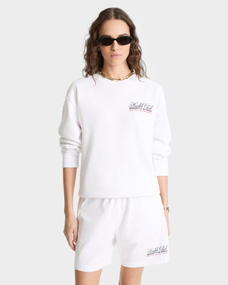 Woman wearing sunglasses, a white Made In USA Crewneck - White/Navy/Fire Red (100% cotton), and matching white shorts with small red text on both pieces.