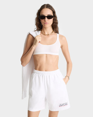 Woman in sunglasses and white sportswear wears the Made In USA Gym Short - White/Navy/Fire Red with a drawstring waistband, holding a jacket over her shoulder against a plain background.