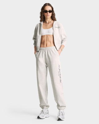A woman stands confidently in NY Health Club Sweatpant - Heather Gray/Navy, paired with a zip-up hoodie, sports bra, sneakers, and sunglasses.