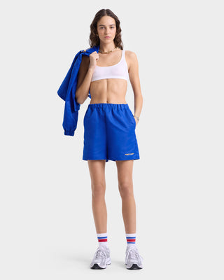 Model wearing blue nylon shorts with an elastic waistband, a smooth woven finish, and gold 'Sporty & Rich' text near the left hem.