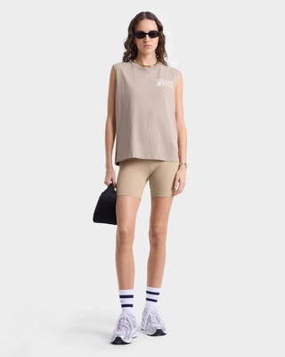 Model wearing tan, ribbed sleeveless T-shirt with a white 'Sporty & Rich Running Club 1994' graphic on the left chest and a crew neckline.