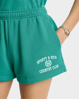 Person is wearing Varsity Crest Soft Disco Short in Spring Green/White, featuring an elastic waistband and Sporty & Rich Country Club text, paired with a gold watch.